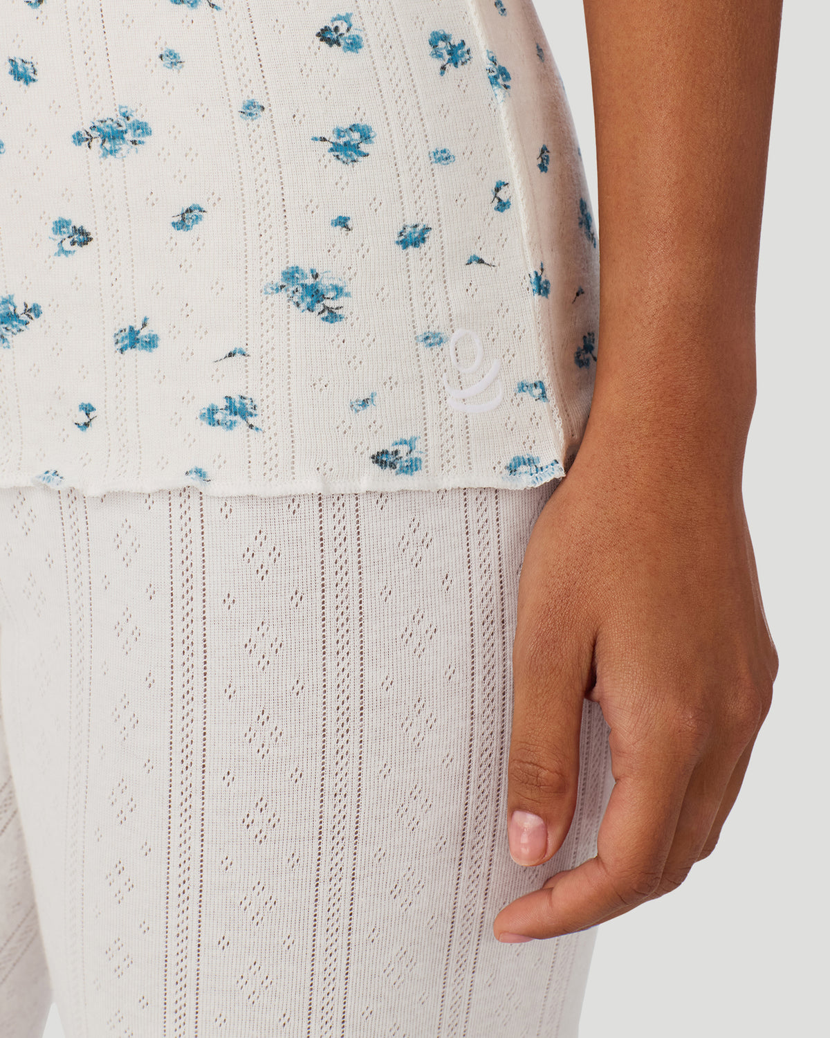 Blue Ditsy; Model is wearing a size S. She is 5’7”, Bust 32”, Waist 25”, Hips 34”.  @ A lady wearing Blue Ditsy Cotton Pointelle Tank in a front view closer look of the bottom hem