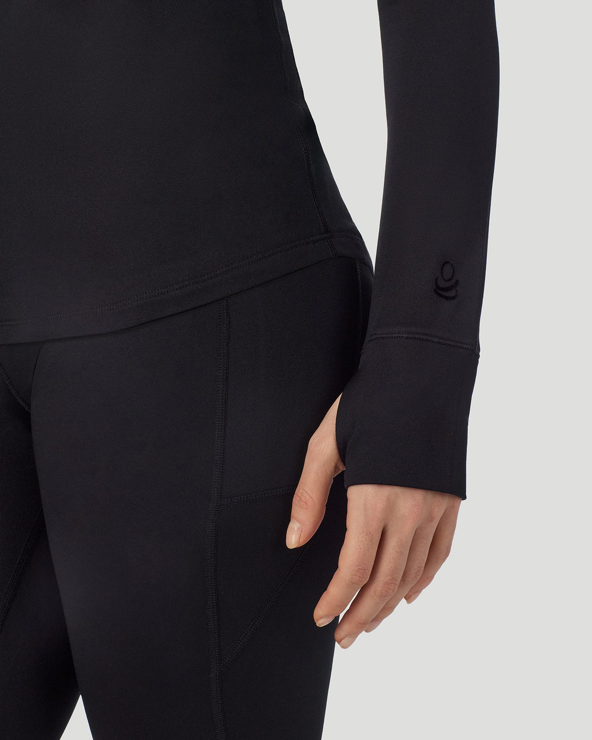 A lady wearing Thermawear Long Sleeve Raglan Crew in black shown in a front view close up detail of the sleeve thumbhole