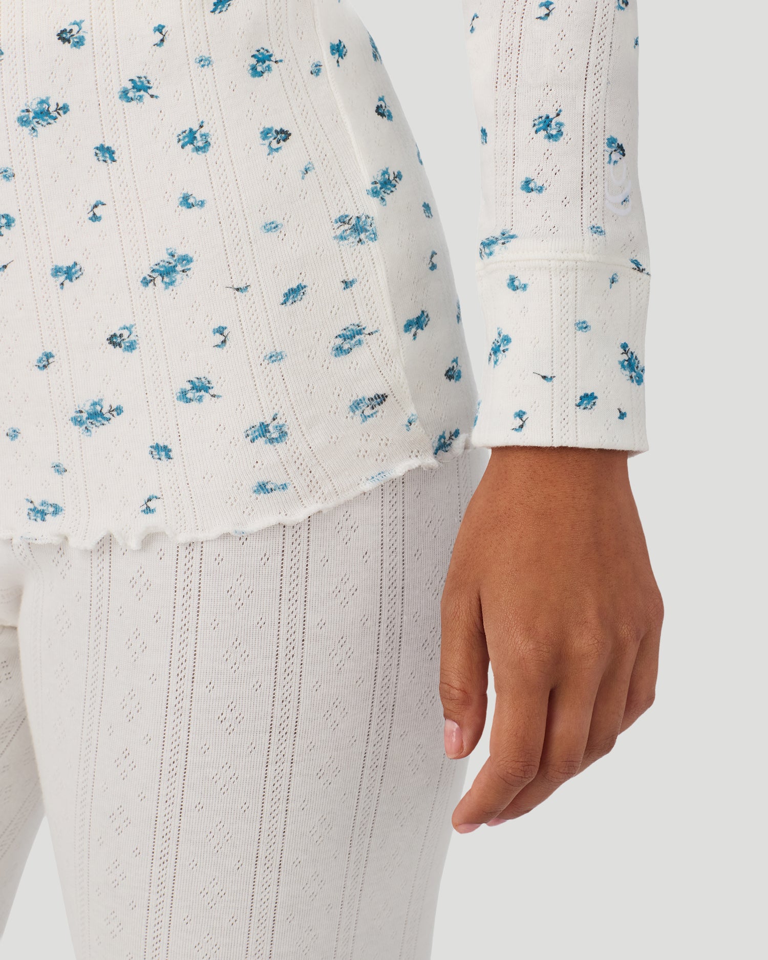 A lady is wearing Blue Ditsy Cotton Pointelle Long Sleeve Henley in a front detail close up look of the sleeve hem