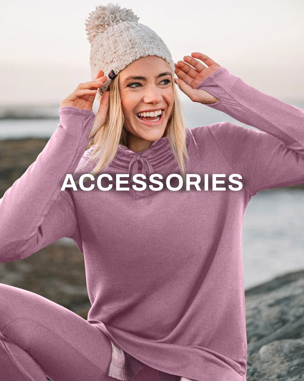 A woman outdoors wearing a mauve-purple knit long-sleeve top and matching pants, with a light beige knit pom-pom beanie. Large white text reading 'ACCESSORIES' is overlaid across the center.
