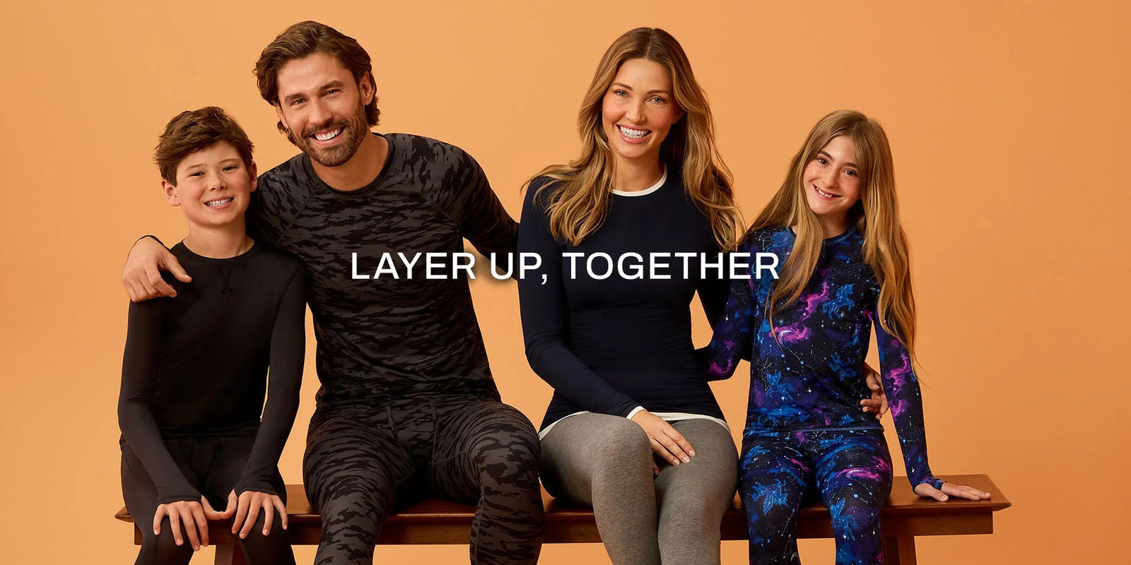 A family of four posing together on a wooden bench against a solid orange background, wearing matching activewear sets. The text 'LAYER UP, TOGETHER' is overlaid in the center.