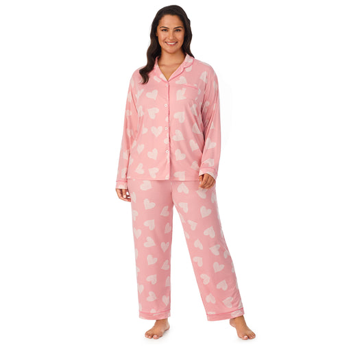 Pink Ground Hearts; Model is wearing size 1X. She is 5’11”, Bust 38”, Waist 34”, Hips 46”. @A lady wearing a pink long sleeve notch pajama set plus with white heart pattern.