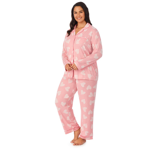 Pink Ground Hearts; Model is wearing size 1X. She is 5’11”, Bust 38”, Waist 34”, Hips 46”. @A lady wearing a pink long sleeve notch pajama set plus with white heart pattern.